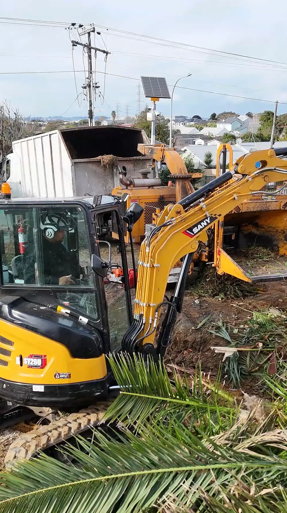 Tree Action digger working beside the chipper and truck on a residential site