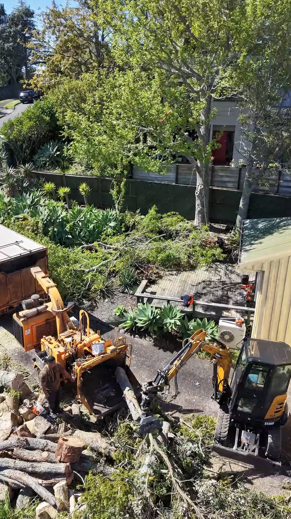 Aerial view of a Tree Action stump grinder and digger working among cut logs in a garden
