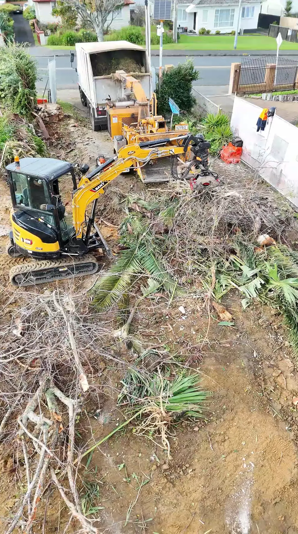 Aerial view of a Tree Action truck, stump grinder and digger clearing a section beside an Auckland street